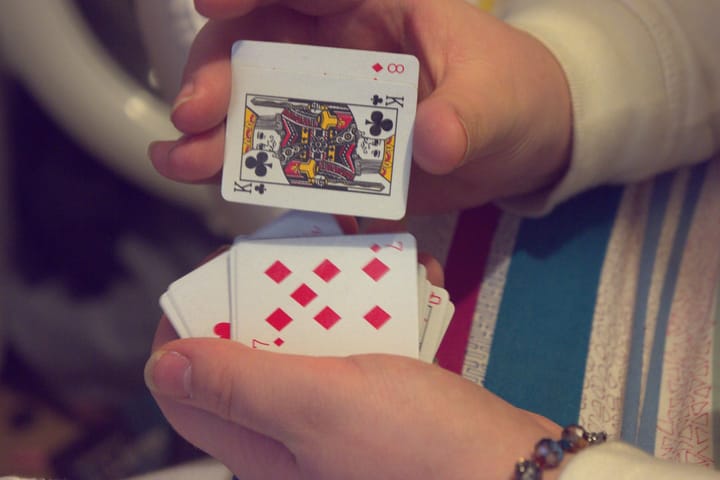 A pair of hands shuffle a tiny deck of playing cards. The king of spades and 7 of diamonds is showing.