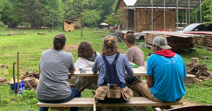 Five people sitting at a picnic table facing away from the camera, looking up into the sky on a rainy day.