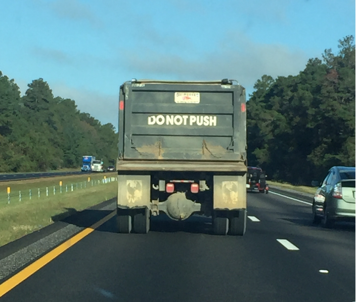 A dump truck with DO NOT PUSH painted in white on the tailbed drives on the interstate.